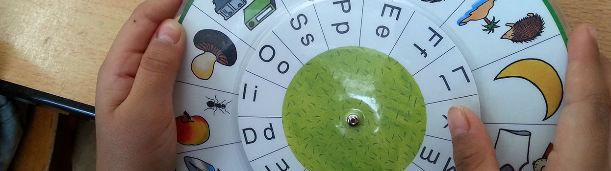 Ein Schulkind hält eine Drehscheibe. Auf dieser Drehscheibe sind Bilder und Anfangsbuchstaben, welche korrekt zugeordnet (gedreht) werden müssen.