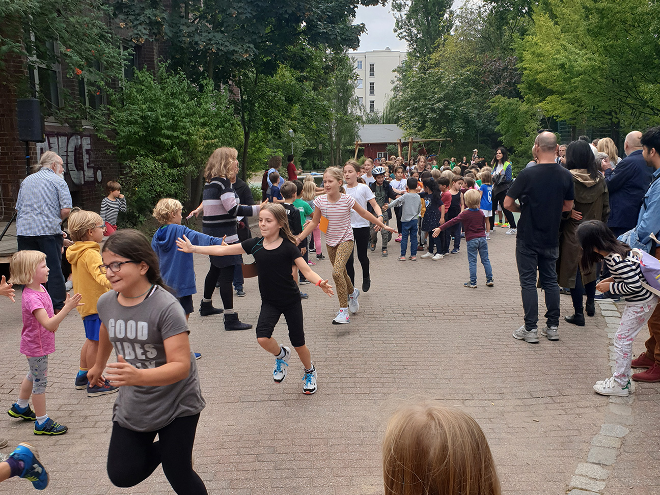 Auf dem Schulhof findet eine Schulveranstaltung statt. Kinder rennen mit viel Freude über den Schulhof.