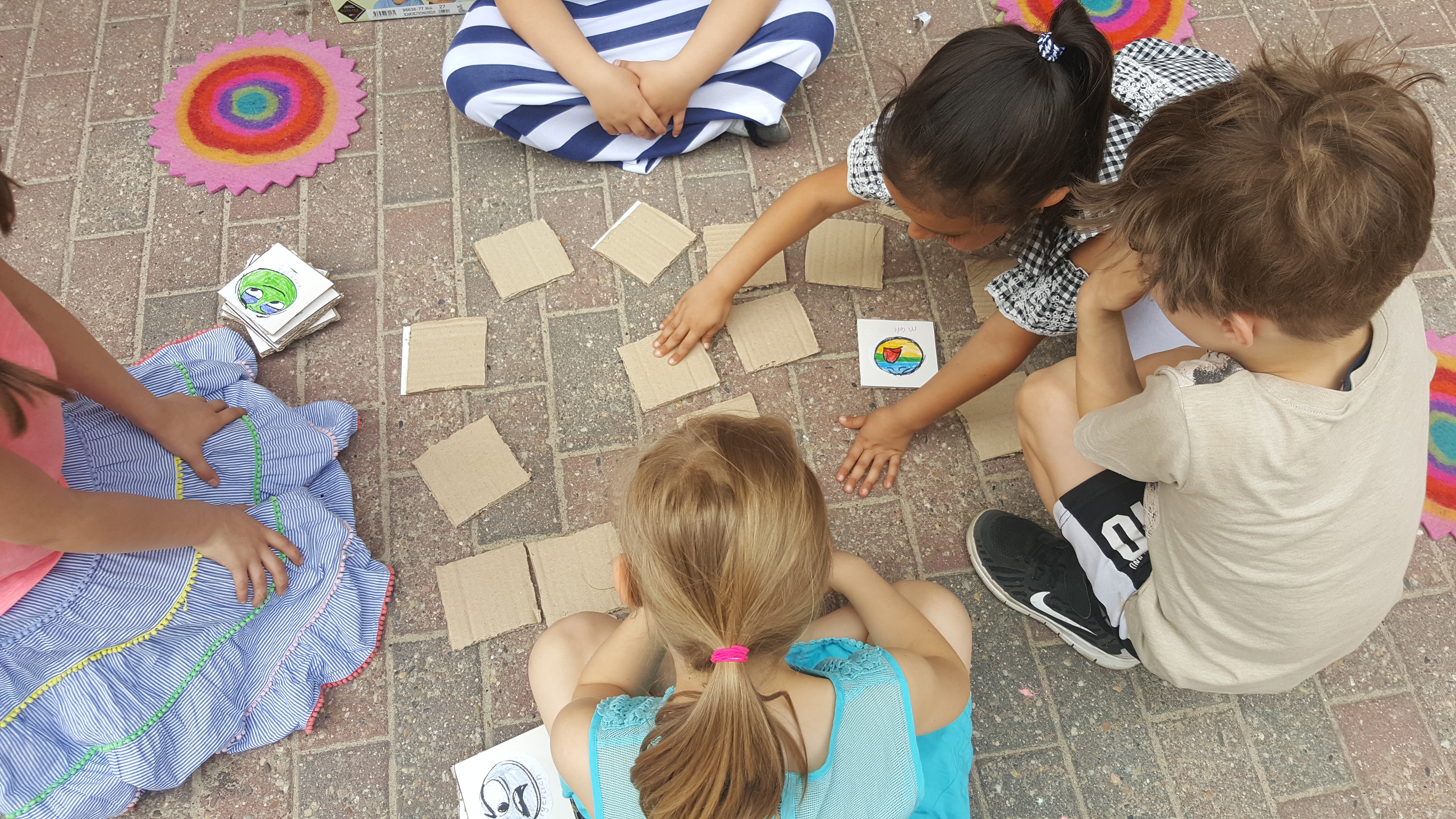 Fünf Kinder spielen Memory. Das Memory ist aus Pappe und selbst gemalten Bildern.