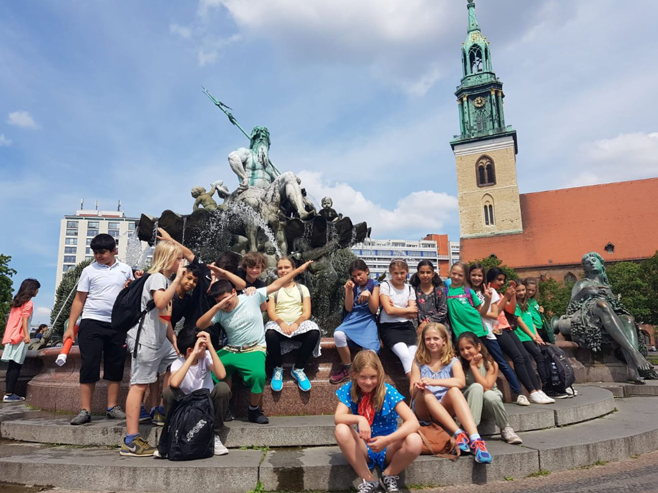 Ein Klassenausflug zum Alexanderplatz. Für das Gruppenfoto hat sich die Gruppe vor dem Neptunbrunnen versammelt. Ein paar Schüler machen dabei faxen.